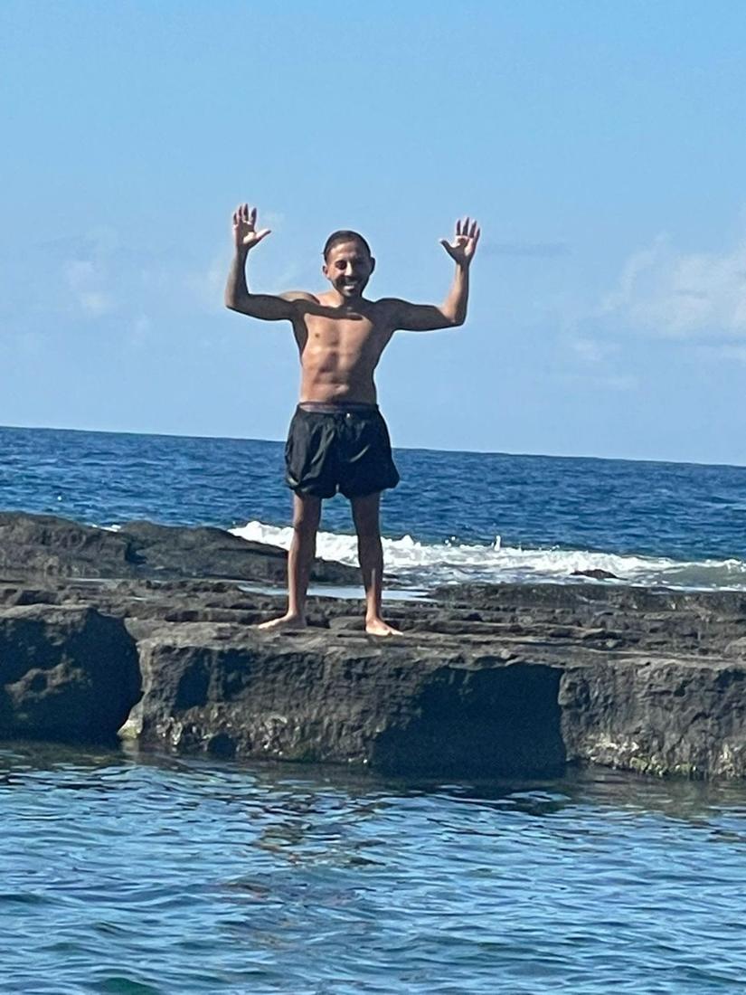 Alpa Abi with raised arms on a rock by the sea